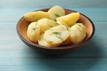 Young boiled potatoes with dill in bowl on light blue wooden table, closeup