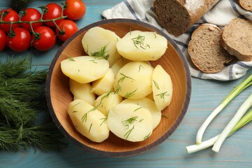 Young boiled potatoes with dill in bowl among products on light blue wooden table, flat lay