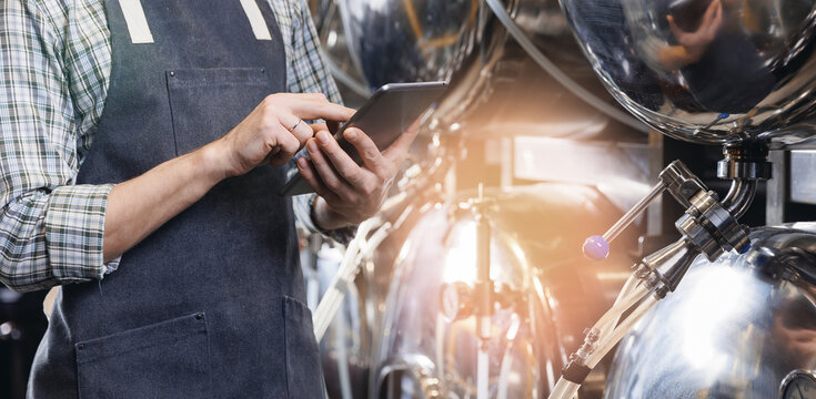 Banner beer factory, worker in apron use tablet computer control indicators of equipment of drink tank in brewery - Powered by Adobe