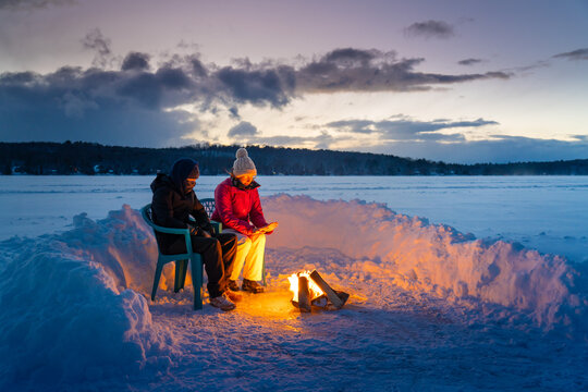 Mom Sitting With Son by Winter Campfire on Frozen Lake Ice