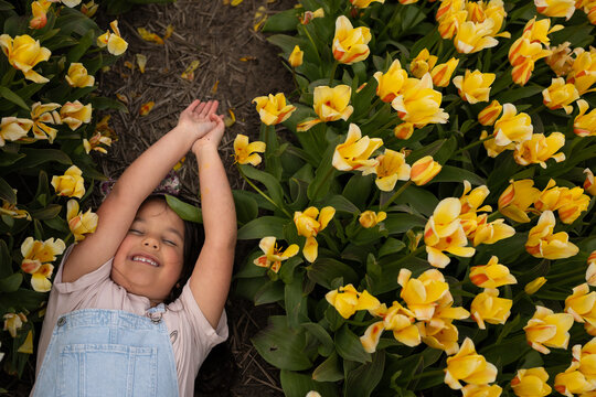Smilling girl lying in camo of yellow tulips