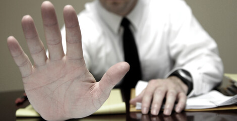 Business Man at Desk Holding Up Hand to Stop Communication