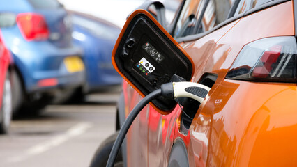 Close up of modern EV electric vehicle car plugged in at charging station