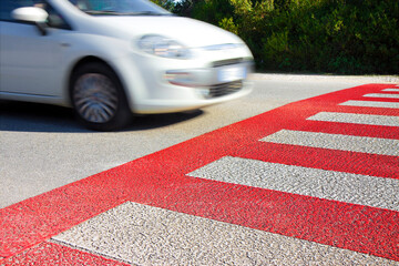 Red and white pedestrian crossing with car on background