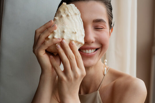 Happy woman hides her eye with a seashell