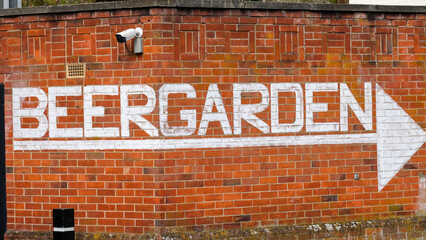 Graffiti white spray painted beer garden sign with directional arrow on old red brick wall at pub