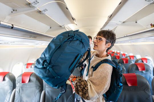 Woman placing bag in overhead bin.