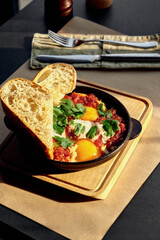 Shakshuka with tomato sauce, hummus, greens and toasts in skillet