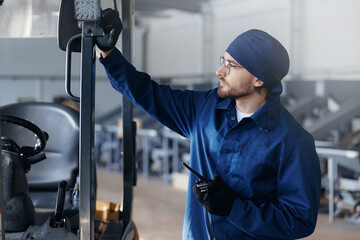 Driver of forklift talking on walkie talkie on warehouse, concept communication of people on industry workplace