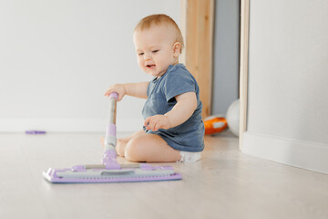 Happy young boy sitting on floor and holding mop for washing. Concept house helper from diapers