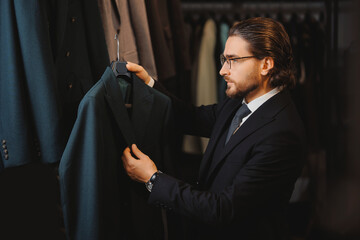 Smiling businessman in glasses chooses to buy suit jacket in classic clothes shop store for men