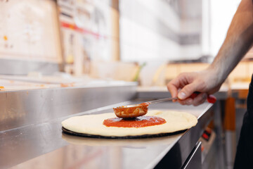 Pizzamaker applies tomato sauce on dough, worker preparing fresh food pizza. Business pizzeria...