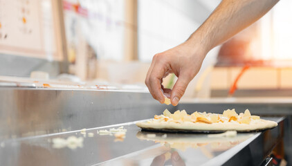 Pizzamaker worker preparing fresh food pizza adds toppings with mozzarella cheese, top view. Business pizzeria concept.
