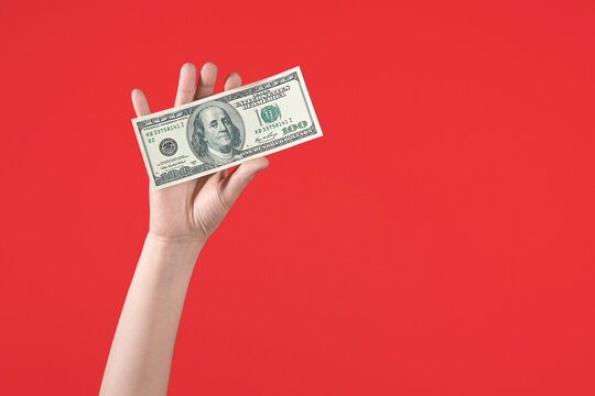 Female hand holding one hundred-dollar bill on bold red background.