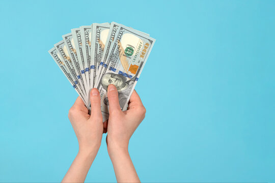 Female hand holding one hundred-dollar bills on blue background.