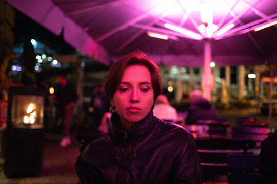 Woman in thought at a neon-lit outdoor seating area