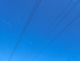 Diagonal hanging high-voltage transmission power lines against blue sky with clouds and shining sun. Empty space. Above-ground electric grid simple background