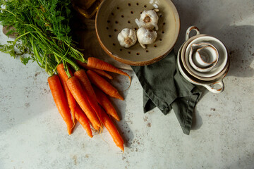 Overhead image of bunched leafy carrots and garlic with kitchenware
