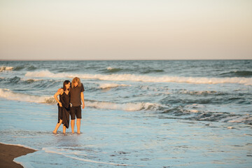 Cheerful loving couple walking along the ocean coastline at sunset