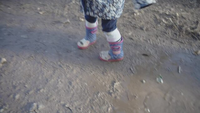 Female child in cat wellies splashing in puddles on a muddy ground on a sunny day