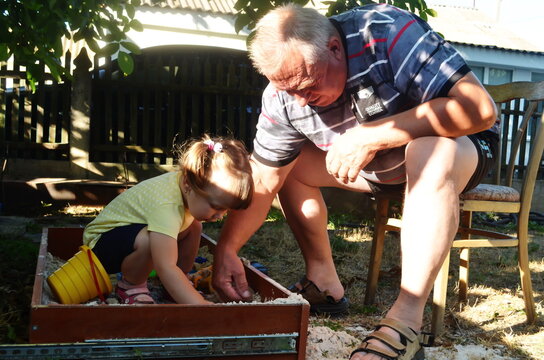 grandfather and little granddaughter are sitting in the sandbox