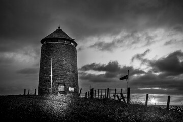 Black and white photo of an old windmill tower by the sea at night