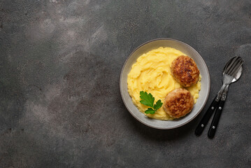 Mashed potatoes with two cutlets in a bowl on a dark background. View from above.