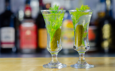 Shaken vodka and pickle juice with ice in a shot glass and garnished with small pickled cucumber and dill
