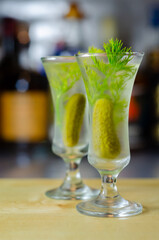 Shaken vodka and pickle juice with ice in a shot glass and garnished with small pickled cucumber and dill
