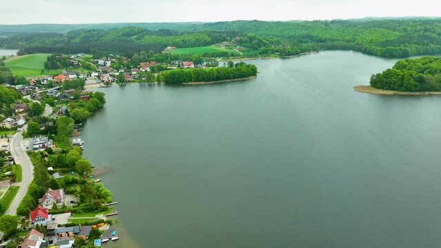 An aerial view of a lakeside town with houses lining the water's edge and lush green hills in the background