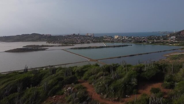 Aerial revealing shot showing salinas of pampatar in Venezuela during sunny day. Salt lake beds with city in background. Wide shot.