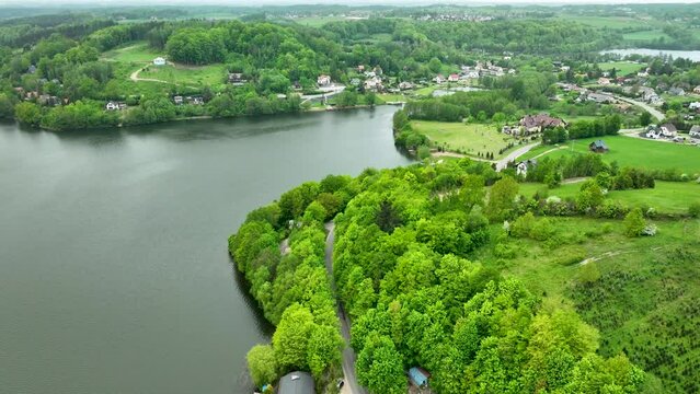 A broad aerial view of a lakeside town surrounded by green hills, showing houses, roads, and a tranquil lake.