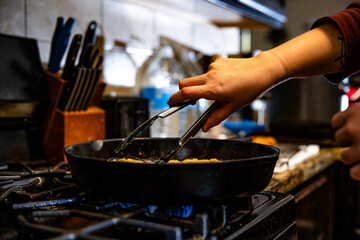 Person stirs an egg in a skillet with tongs,