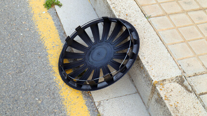 Lost hubcap from a car wheel lies on the side of the road.