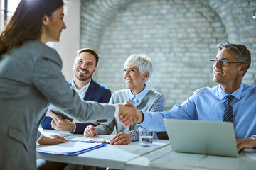Happy member of human resource team shaking hands with female candidate on job interview in the office.