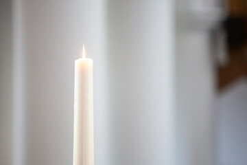 A solitary white candle burning brightly in a calm and cozy atmosphere, evoking peace and...