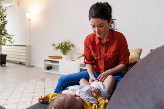 woman changing diaper of daughter on sofa