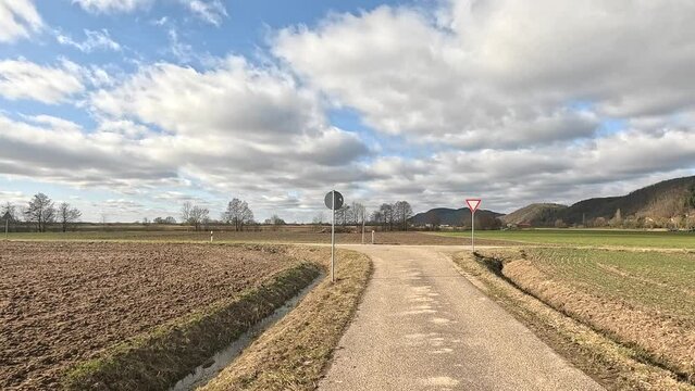 Narrow paved road pssing through plowed and green fields in the countryside on a sunny day