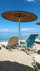 A straw parasol and sun loungers on the sandy beach of the Olympic Riviera overlooking the...