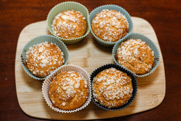 six muffins are shown in cupcake cases on a wooden board