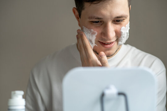 Man applying cleaning or shaving foam on his face in front of mirror