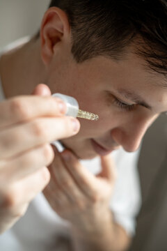 Close uo of a young man applying cosmetics to his face with a pipette