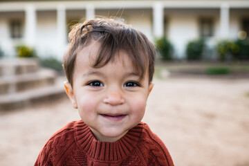 Two year old happy toddler boy with dark hair is camera aware and looks at the camera happily