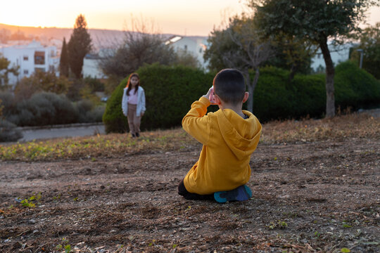 Brother Photographs Sister At Sunset In Park.
