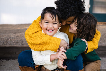 Brunette mother and her adorable children embrace lovingly while sitting outside