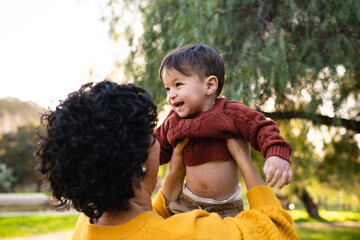 Adorable toddler boy is lovingly held by adoring mother outside at sunset