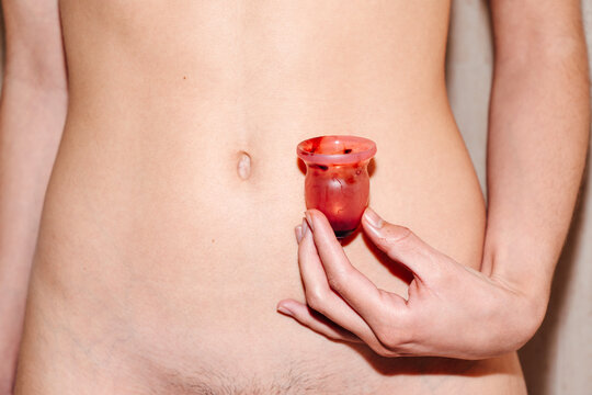 Naked woman holding menstrual cup with period blood