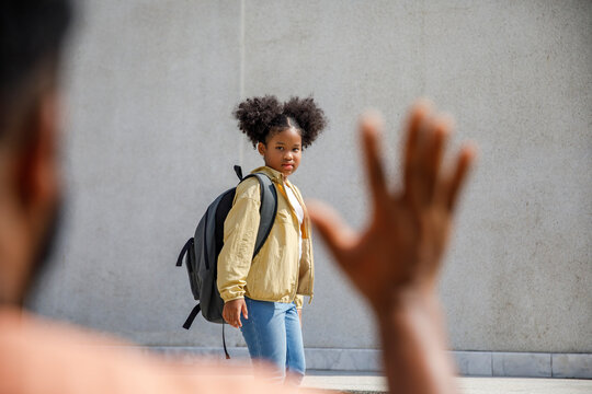 Girl with backpack looking at father waving hand
