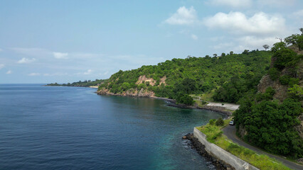 Fototapeta premium Car drives along the north coastal road between cliffs and the sea in Sao Tome and Principe, Africa