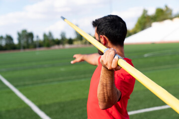 An athletic man throws the javelin in the stadium.